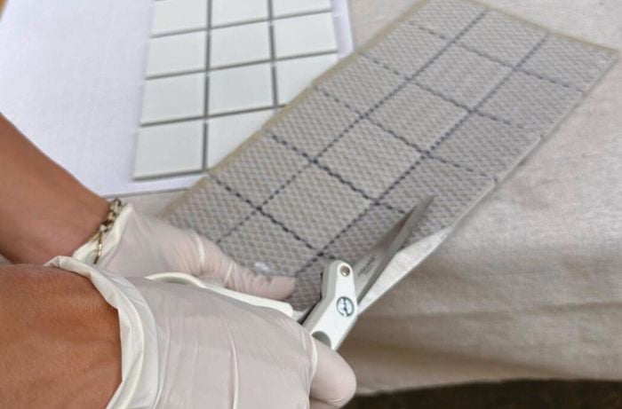 Cutting a grey mosaic tile sheet with white scissors