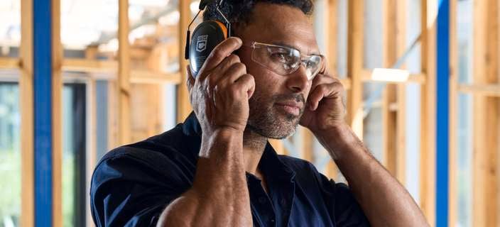                     Person wearing protective earmuffs inside a partially constructed building frame.