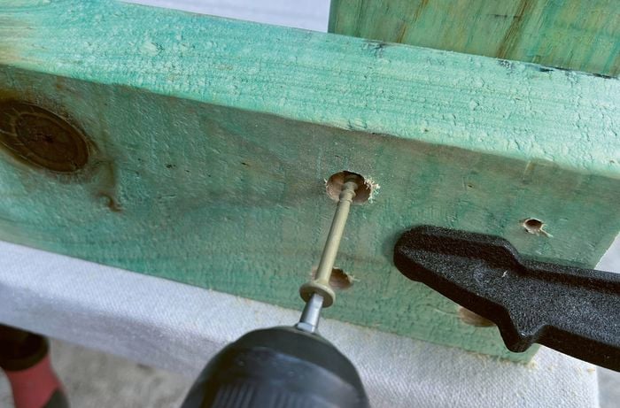 A screw being driven into a piece of treated timber, clamped against another piece