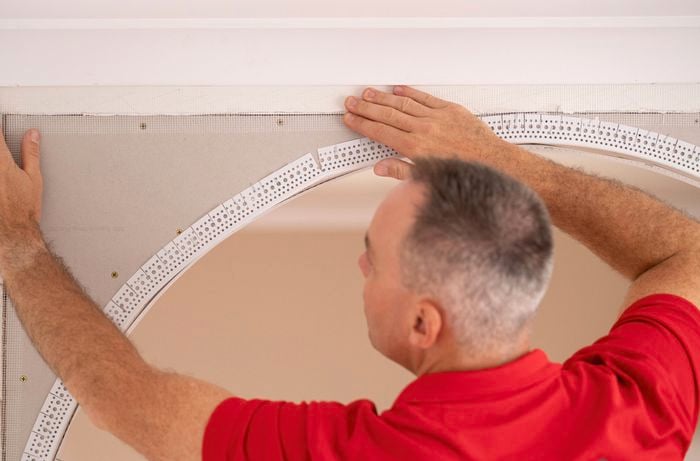 A Bunnings Team Member is pressing joining tape along the joins and over the moulding edges.