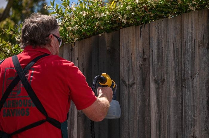 A Bunnings team member painting the fence using a spray gun.