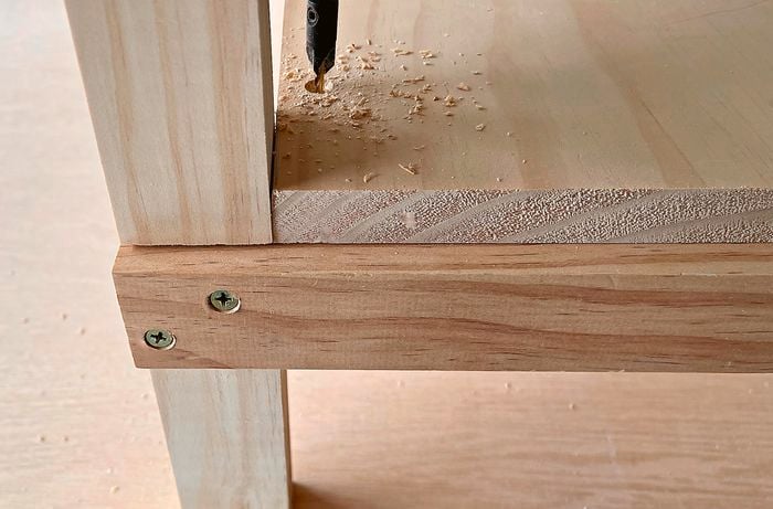 A person securing a shelf panel to a kitchen trolley pine frame using a drill.