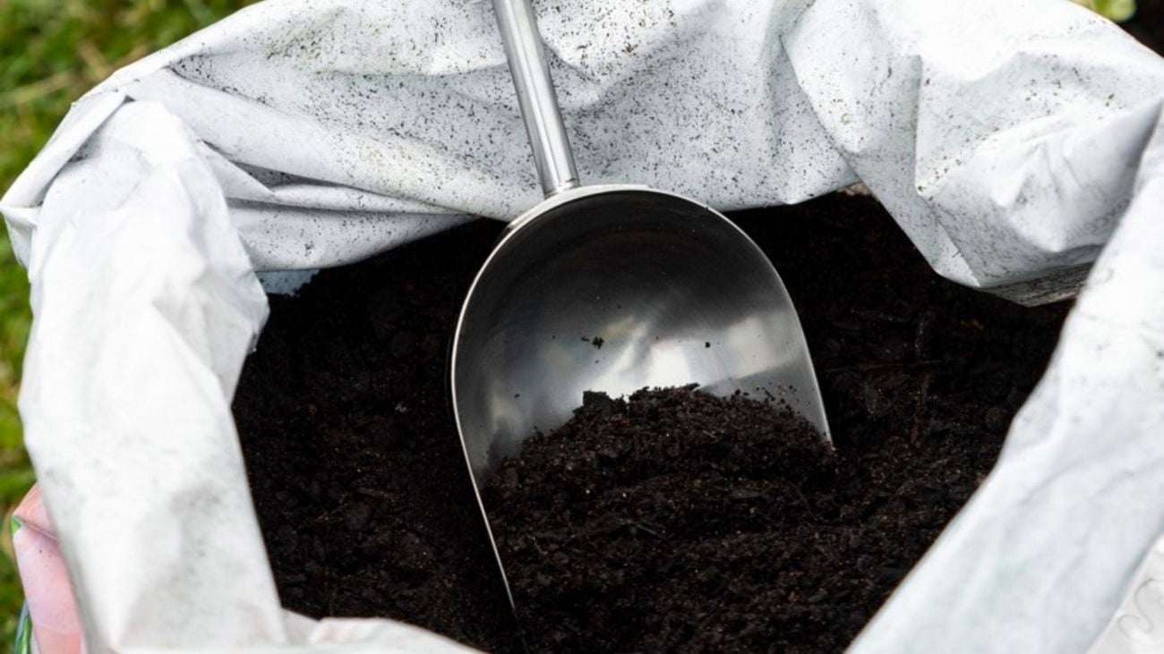 Person kneeling on a garden mat outside, digging in a pot full of soil with a Cyclone garden trowel
