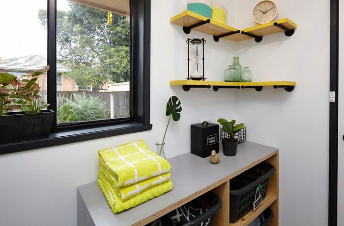 Wider shot of black and yellow corner shelves as part of a black white and yellow themed laundry space with towels, pot plant and laundry baskets