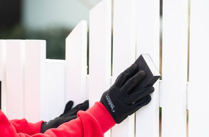 Sanding a white picket fence gate to prepare the surface for painting.