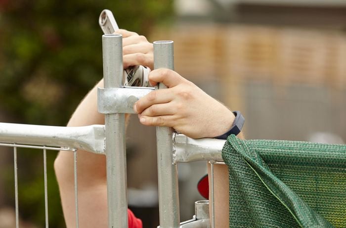 A person joining two sections of temporary fencing using a spanner