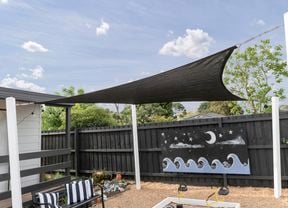 An installed black shade sail over a kindergarten sandpit
