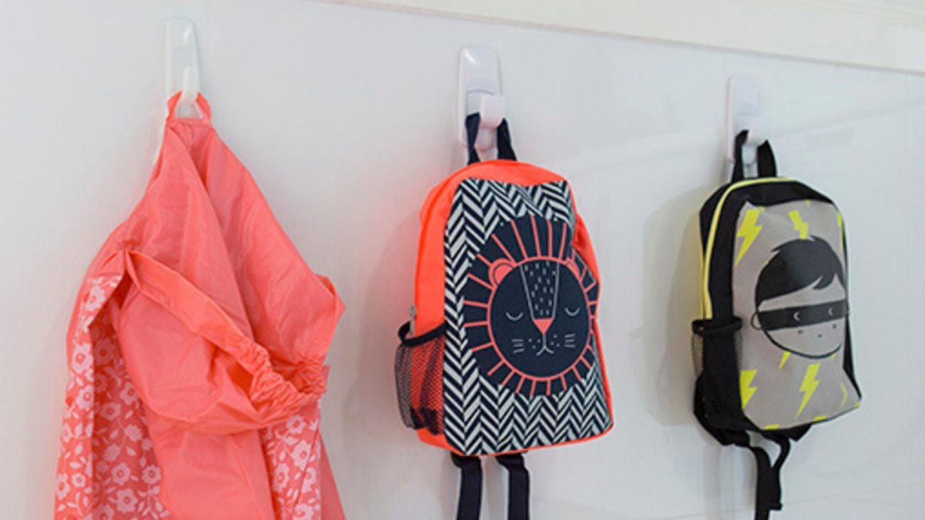 Kids bags and jacket hanging from hooks on a wall.