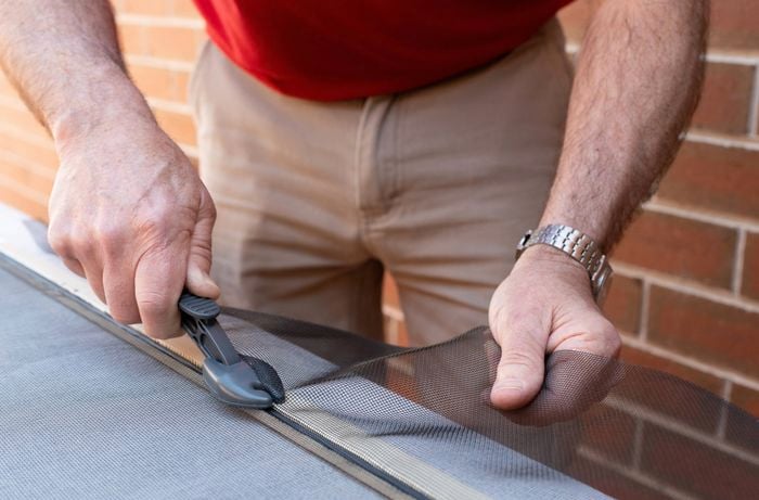A person is trimming the excess mesh using a flyscreen trimmer.