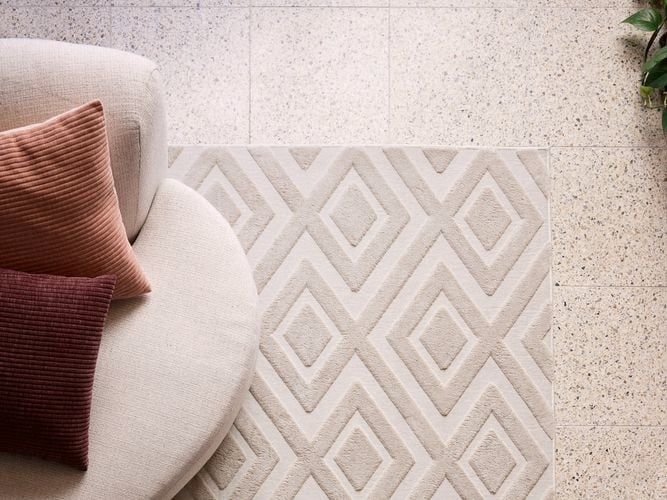 A white couch with two cushions on it, on a rug on laminate flooring.