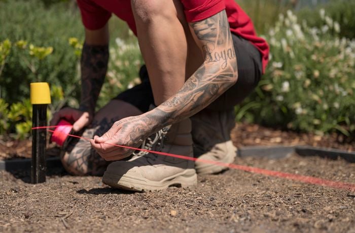 A person wearing red shirt is running a string line between the stakes to outline the shape of your formwork.  