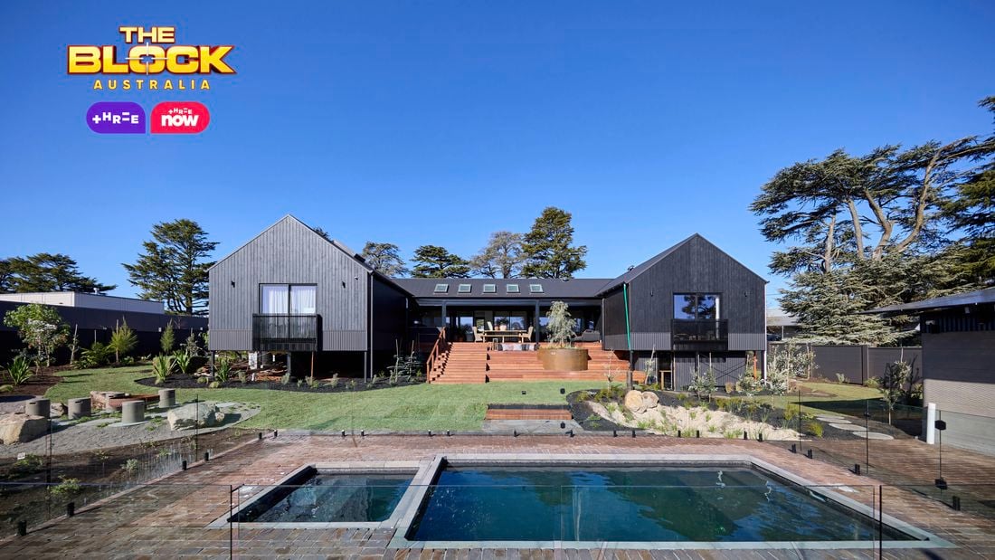 The back of a house with a pool in it, a rocked area, timber decking and many plants in it.