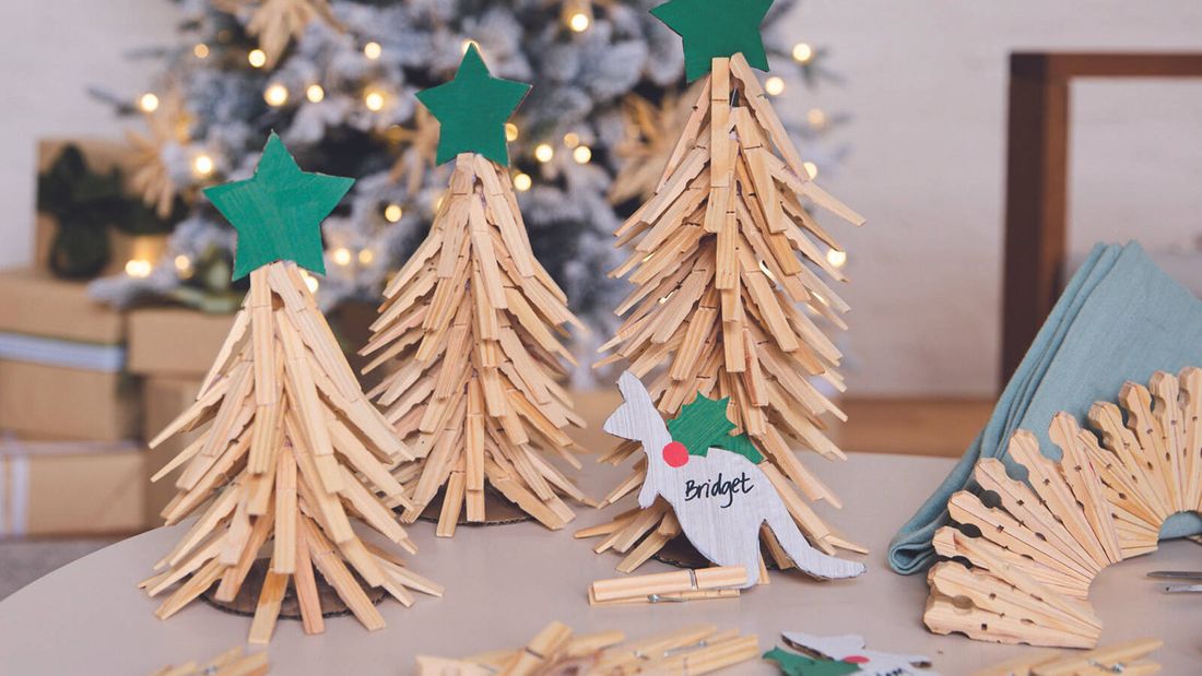 A cardboard kangaroo Christmas table place card with the name ‘Bridget’ written on it, resting in front of miniature wooden peg Christmas trees.