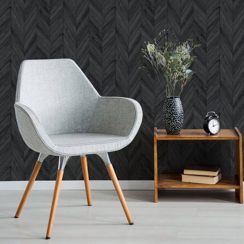 A grey chair with dark grey herringbone wallpaper on the wall.