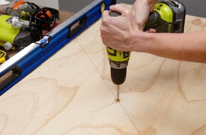 A person drilling a hole through the centre of a panel of plywood