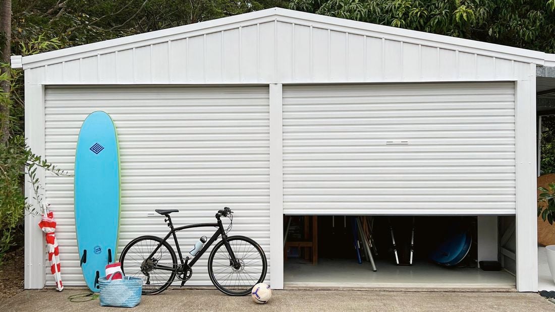 A bicycle, surfing board, ball and a bag in front of a painted garage.