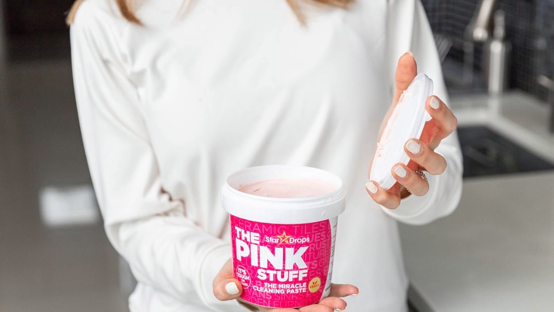 A lady holding a tub of The Pink Stuff with the lid off of the tub.