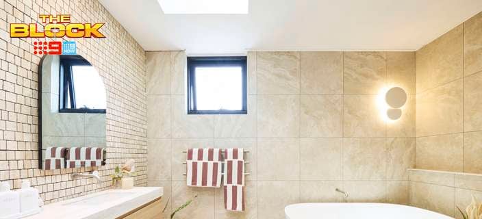 A modern bathroom with a bath in it, towels hanging on the wall, a window, a mirror on the wall, a basin with drawers underneath it.