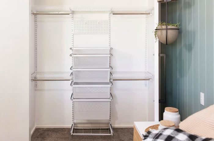 An empty wardrobe with hangers, wire mesh drawers, a pegboard and overhead wire rack