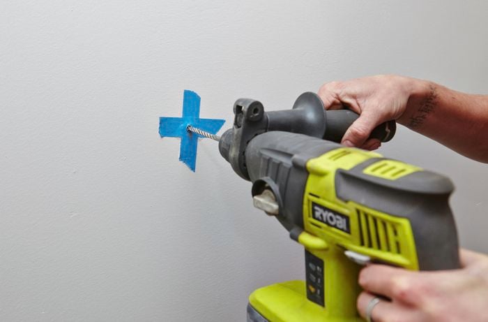 A hole being drilled in a wall at a point marked by masking tape