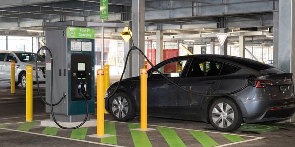 How to use a public EV charging station, demonstrated by a black Tesla parked and charging at a fast EV charger in a multi-level car park.