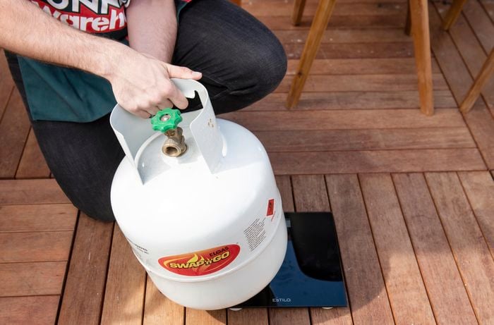 A person weighing a gas bottle on bathroom scales