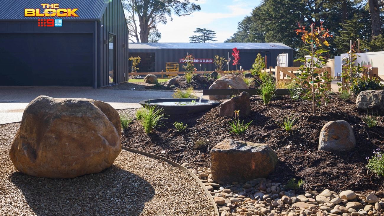 The front area of a house with rocks, shrubs, trees and a driveway in it.