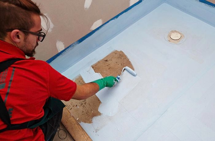 A person applying waterproofing to a bathroom floor with a roller