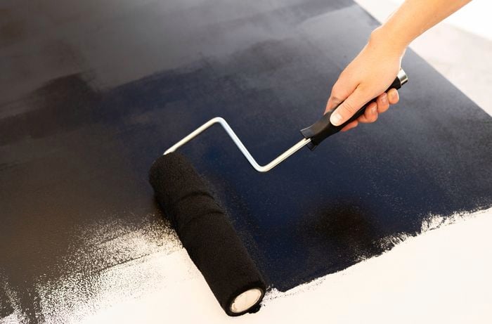 A person is applying chalkboard paint with a paint roller to transform a MDF panel into a chalkboard wall. 