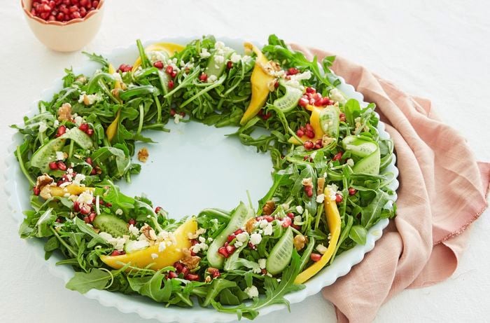 A green salad is arranged in a circle to make a Christmas wreath shape.