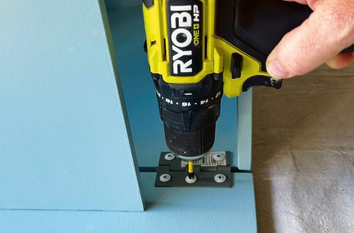 A drill attaching a hinge to a cabinet door.