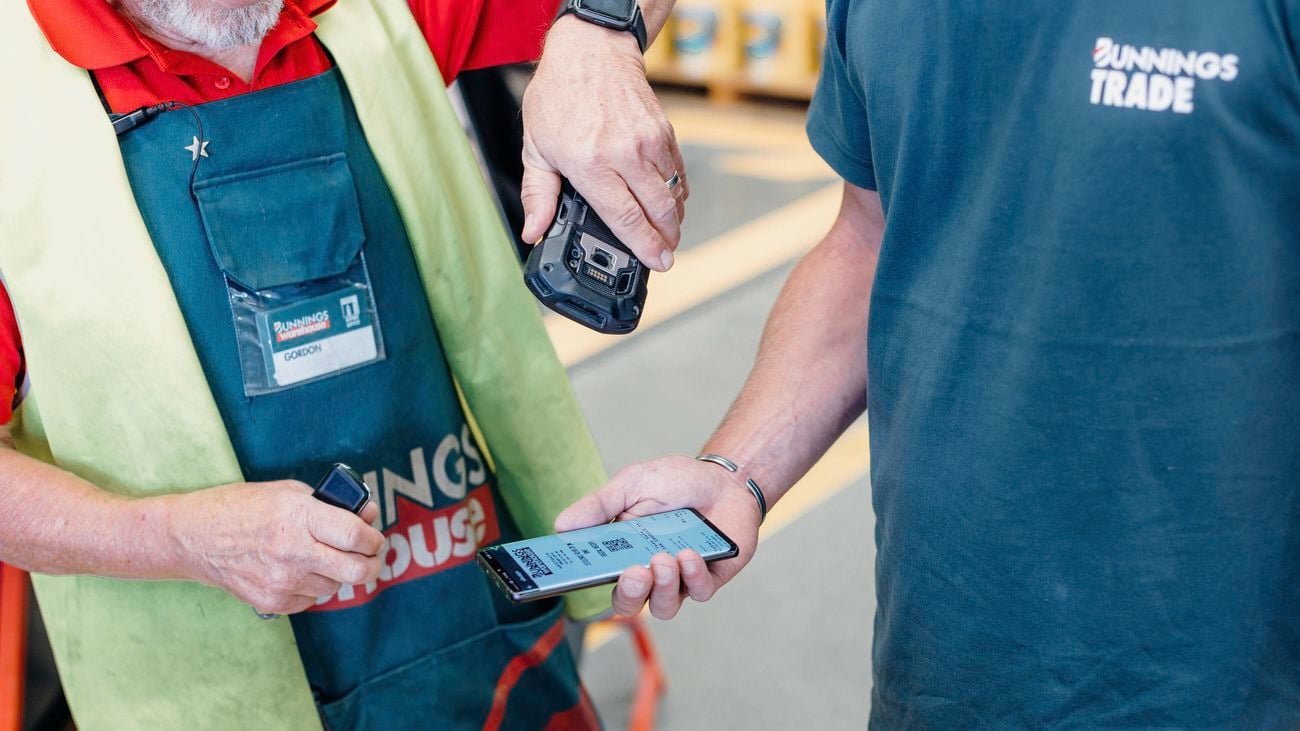 A Bunnings Warehouse Red Shirt team member scans a mobile phone with the Bunnings Trade PowerPass App on it being held by a tradie.