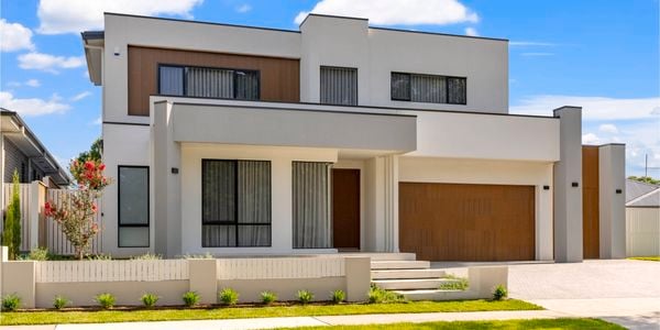 Frontage of a double story home with timber garage door, rendered cream, black metal framed windows and established garden