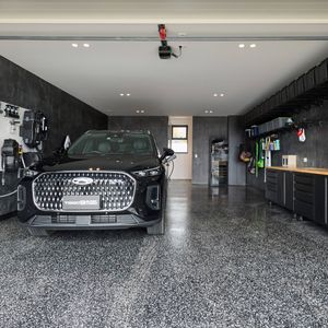 Modern garage featuring a black SUV, polished speckled flooring, wall-mounted storage, bicycles and built-in cabinetry.
