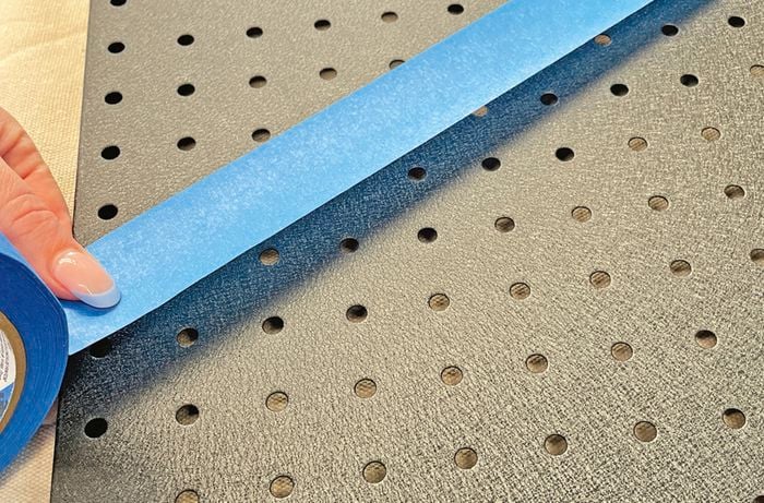 blue painters tape being applied to peg board