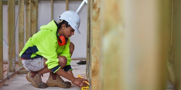 A construction worker measuring the base of a wall frame on a construction site