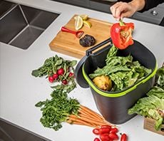 Person placing vegetable food scraps in a small bin for compost