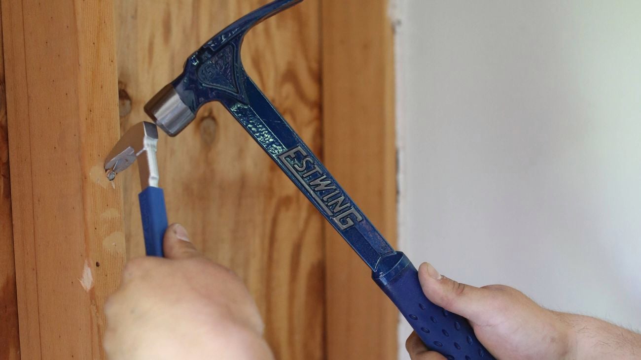 A close up image of two hands holding a Estwing hammer and nail puller pry bar