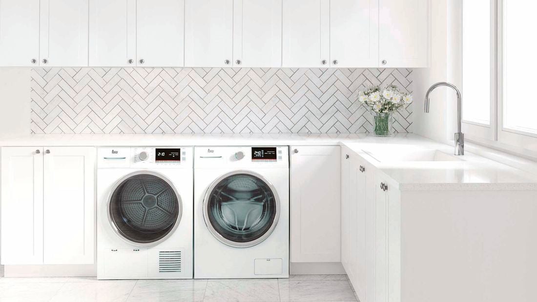 Laundry with white cabinets, white herringbone tiles and washer and dryer.