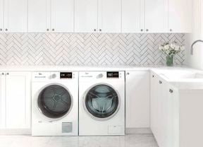 Laundry with white cabinets, white herringbone tiles and washer and dryer.