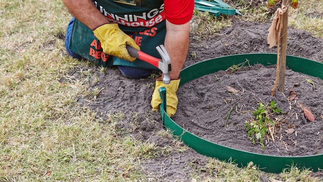 Person hitting a plastic peg with a hammer to secure garden edging.