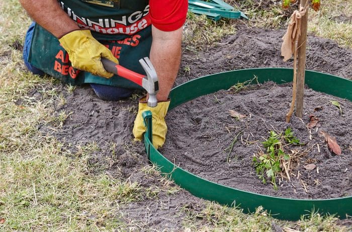 Person hitting a plastic peg with a hammer to secure garden edging.