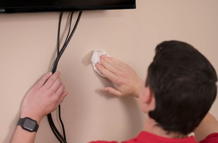 Cleaning the wall while holding cables to the side with the other hand.