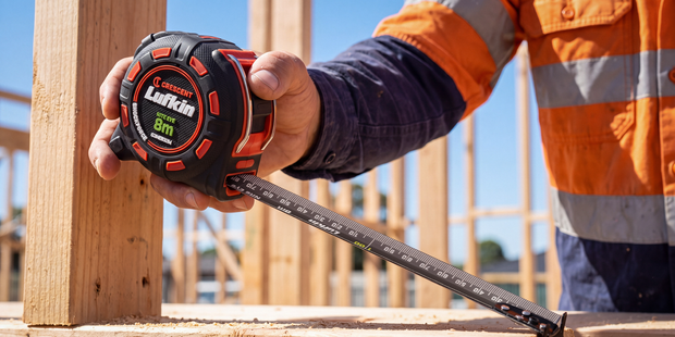 Worker using a Crescent Lufkin 8m tape measure to take measurements within a timber-framed construction site.