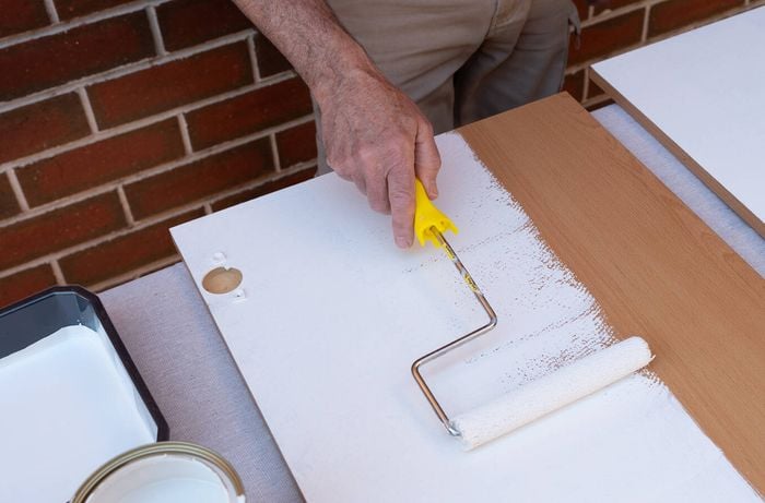 A person is using a paint roller to apply white paint to a cabinet door.