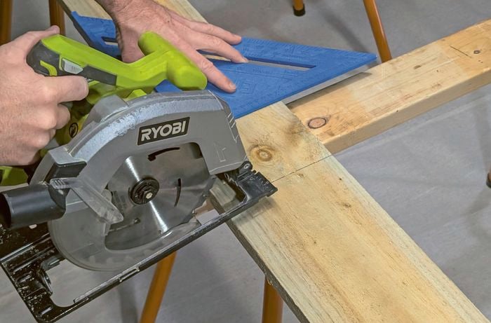 Hands cutting timber with a circular saw and a rafter square.