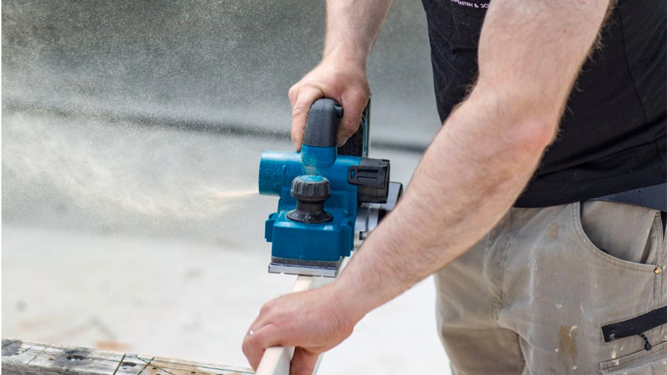 A close-up image of a man’s arms and torso region using a Makita planer