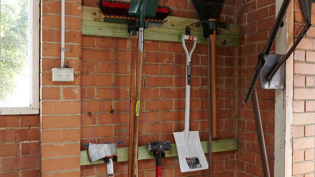 Garden tools hanging from hooks set in timber beams attached to a garage wall