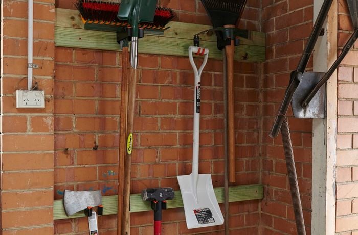 Garden tools hanging from hooks set in timber beams attached to a garage wall
