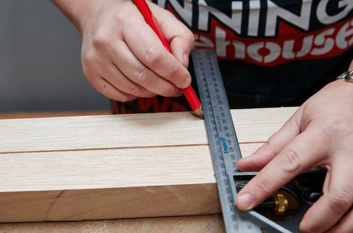 Person using a metal ruler and pencil to mark up two bits of timber.